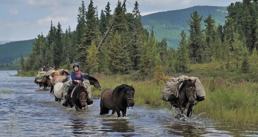 Guests ride alongside the pack horses at the shore of a lake in Mongolia